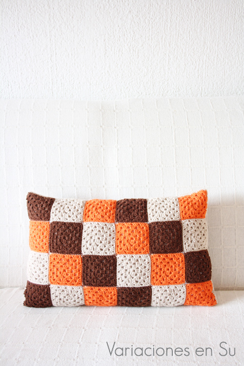 Cojín hecho con granny squares o cuadrados de ganchillo tejidos en lana de colores marrón, naranja y beige.