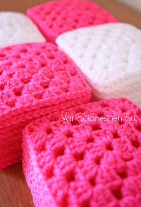 Granny squares o cuadrados de ganchillo tejidos en lana de colores rosa y blanco.