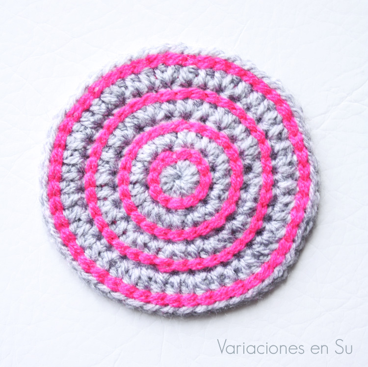 Posavasos de ganchillo, de forma circular y tejido en lana de colores gris y rosa.