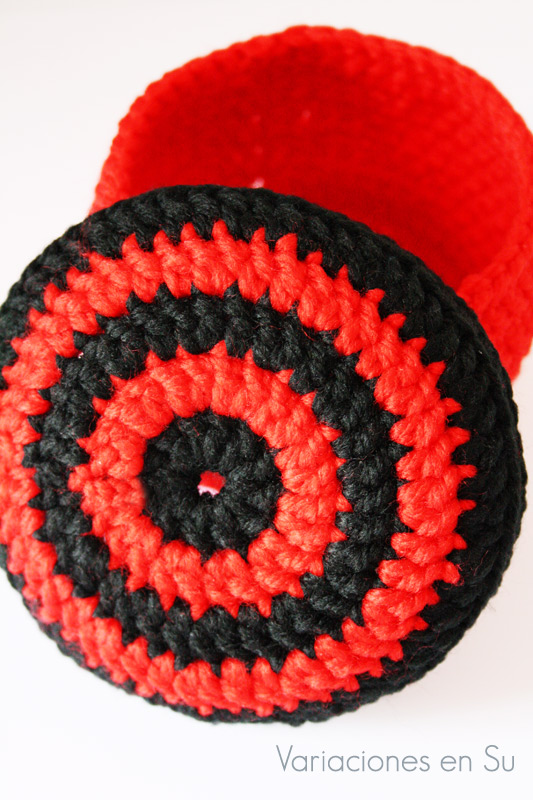 Cesta de ganchillo de forma circular con tapa incluida, tejida en los colores rojo y negro.