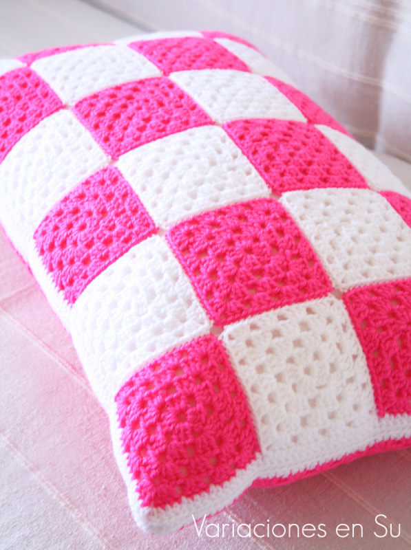 Cojín de ganchillo formado por granny squares o cuadrados, y tejido en los colores rosa flúor y blanco. Detalle de la cara A.
