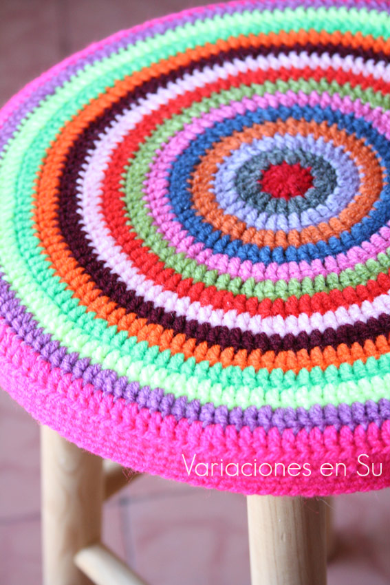 Funda de ganchillo para taburete, de forma circular y tejida en llamativos colores.