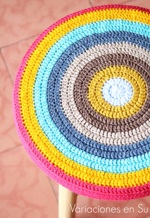 Funda de ganchillo para taburete, de forma circular y tejida en alegres colores.