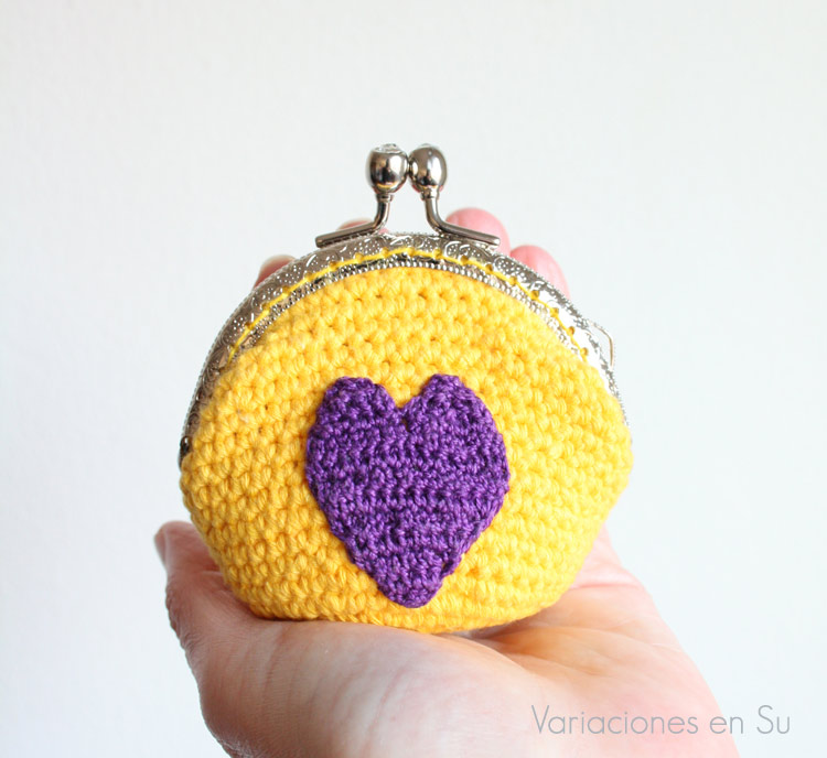 Monedero de ganchillo en amarillo con figura de corazón en violeta. Está acabado con una boquilla metálica plateada con filigrana.