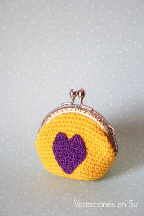 Monedero de ganchillo en amarillo con figura de corazón en violeta. Está acabado con una boquilla metálica plateada con filigrana.