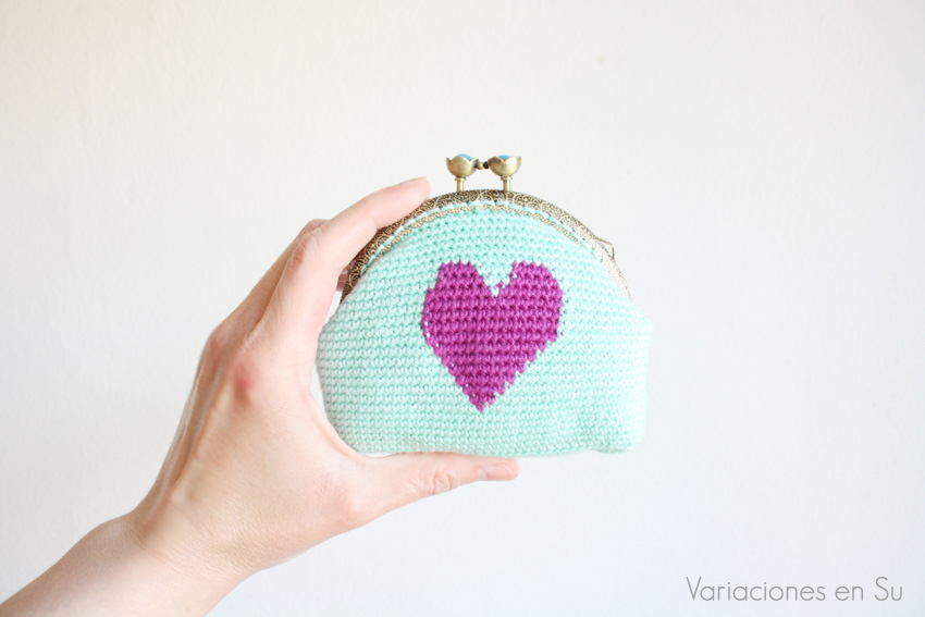Monedero azul con corazón violeta Monedero de ganchillo en azul con figura de corazón en violeta. Está acabado con una boquilla metálica de color bronce con filigrana y cierre en forma de flor.